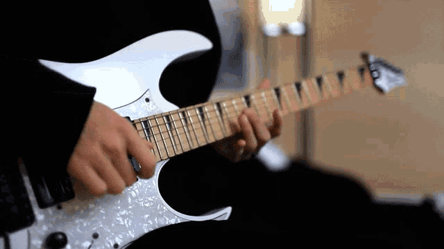a person is playing a white electric guitar with a pearl finish