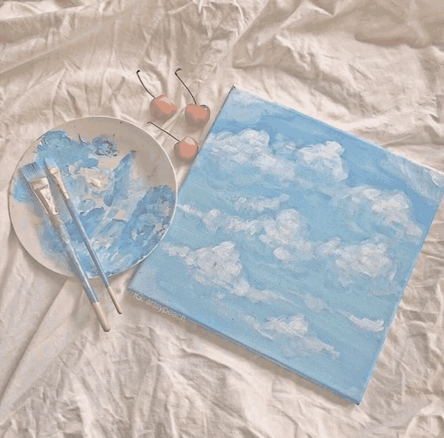 a painting of clouds on a canvas next to a plate of paint