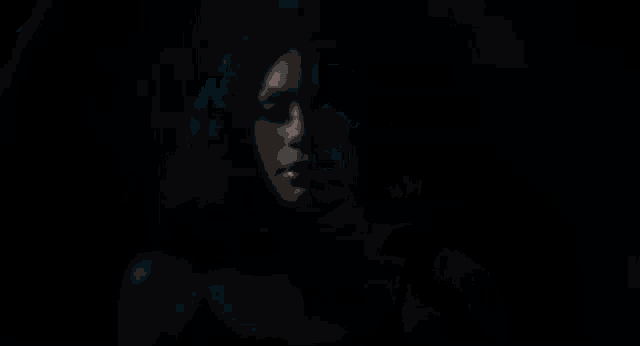a woman in a black tank top and earrings is standing in the dark .