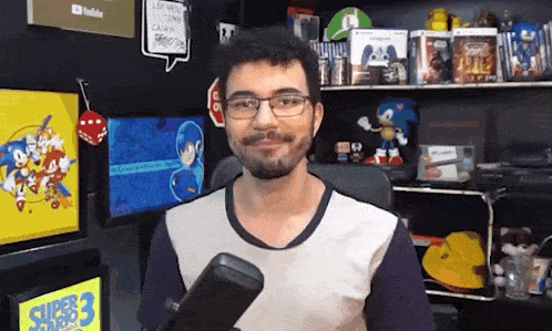 a man with glasses and a beard is holding a microphone in front of a shelf filled with video games .