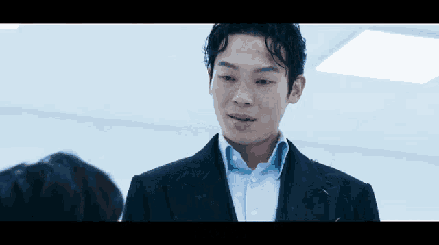 a man in a suit and a blue shirt is standing in a room