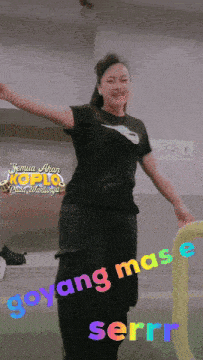a woman wearing a black nike shirt is dancing in front of a sign that says goyang mas e serr