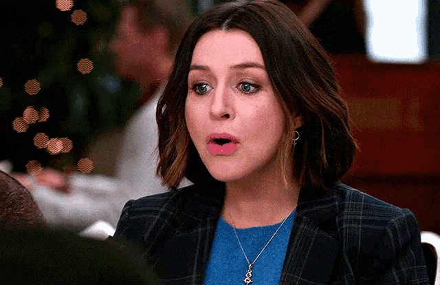 a woman wearing a plaid jacket and a blue sweater looks surprised