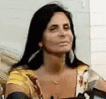 a woman with long black hair is sitting on a couch making a funny face .