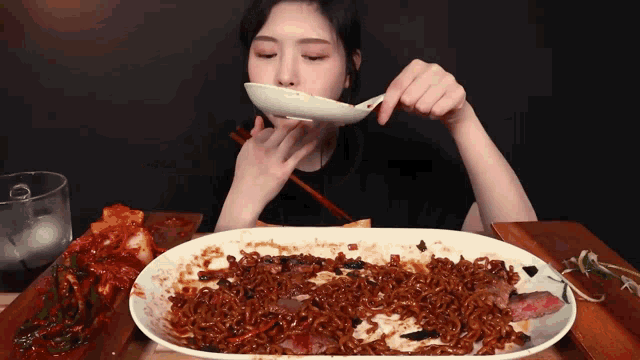 a woman eating noodles with chopsticks and a spoon in her mouth