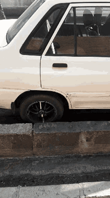 a white car with black wheels is parked on a curb