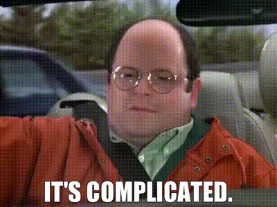 a bald man wearing glasses and an orange jacket is driving a car and says it 's complicated