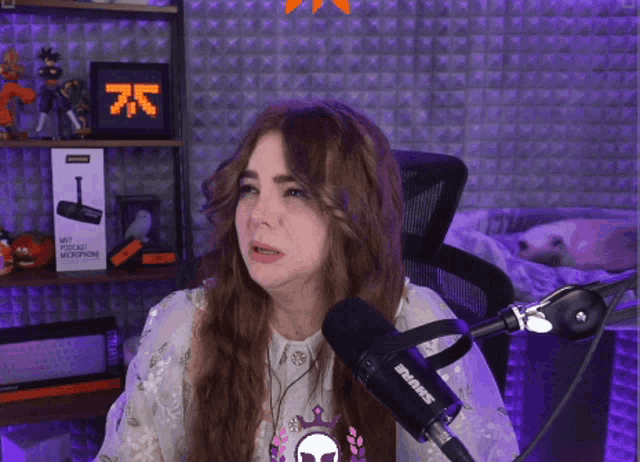 a woman is sitting in front of a microphone with the number 75 on the wall behind her