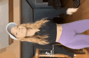 a woman in purple leggings and a black crop top is dancing in a room .