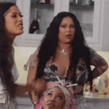 two women are standing next to each other in a kitchen talking to each other .