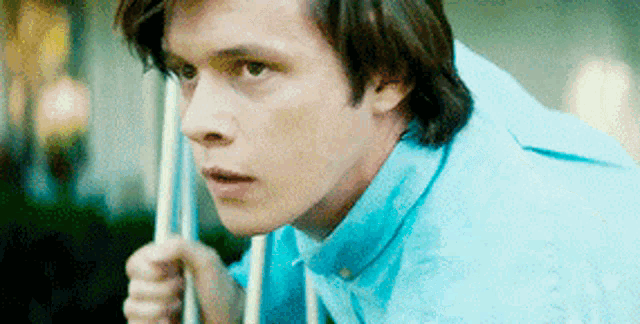 a man in a blue shirt is holding a pool cue and looking at the camera .