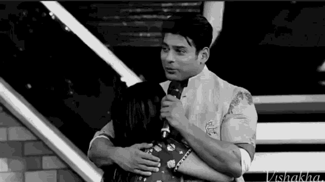 a black and white photo of a man hugging a woman while holding a microphone .