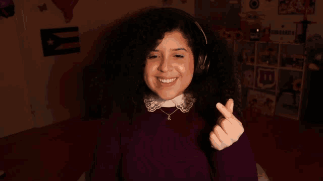a woman wearing headphones is smiling and making a heart shape with her hand