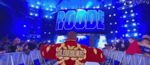 a man in a red robe with the word glorious on the back walks through a wrestling ring .