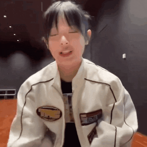 a young man wearing a white jacket and a black shirt is making a funny face .