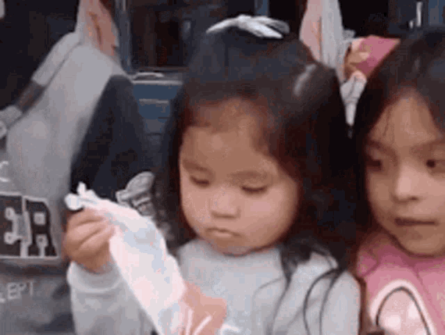 two little girls are sitting next to each other on a bus and one of them is holding a piece of paper .