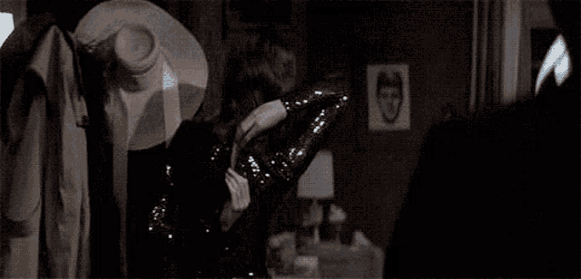 a woman in a black dress is standing in a dark room holding a hat .