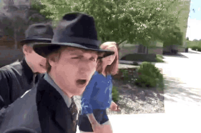 a man wearing a fedora stands next to two other people