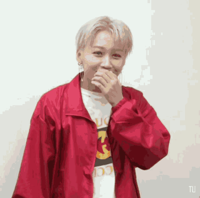 a woman wearing a red jacket and a gucci shirt is covering her mouth