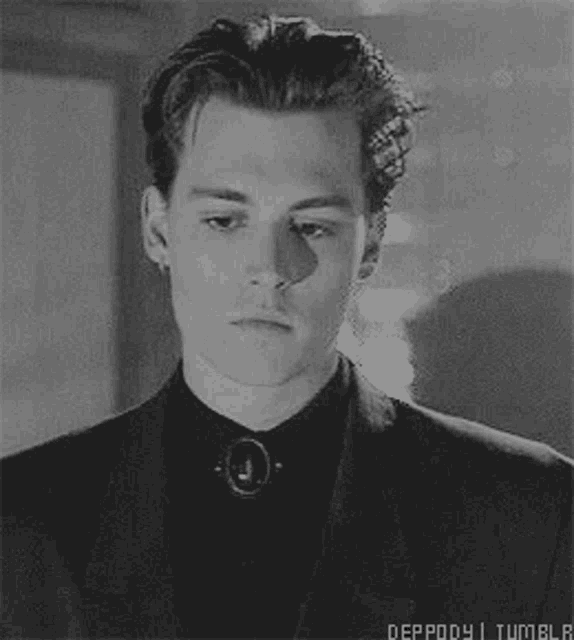 a black and white photo of a young man wearing a suit and a black shirt .