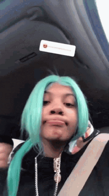 a woman with green hair is sitting in a car with a sticker on the ceiling .