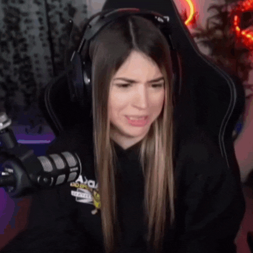 a woman wearing headphones and a hoodie is sitting in front of a microphone .