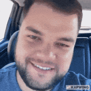 a man with a beard is smiling while sitting in the back seat of a car