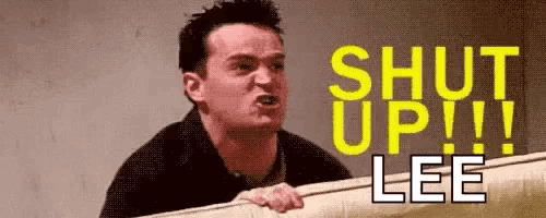 a man is peeking over a wall and yelling at someone with the words `` shut up !! lee '' .
