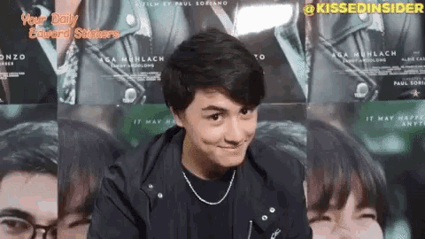 a young man making a funny face in front of a wall of movie posters