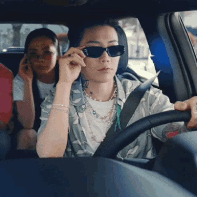 a woman wearing sunglasses is driving a car while another woman talks on a cell phone