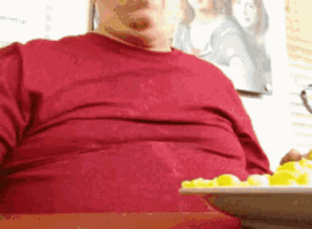 a man in a red shirt is sitting at a table with a plate of food on it