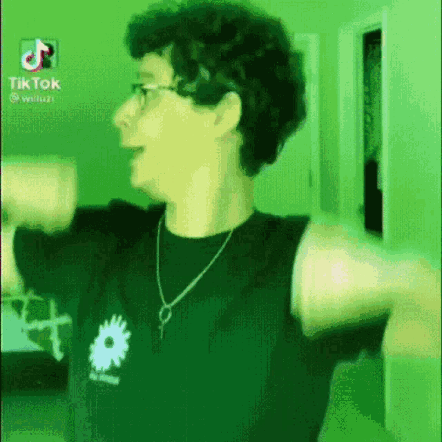 a man with curly hair and glasses is wearing a black shirt and a necklace .