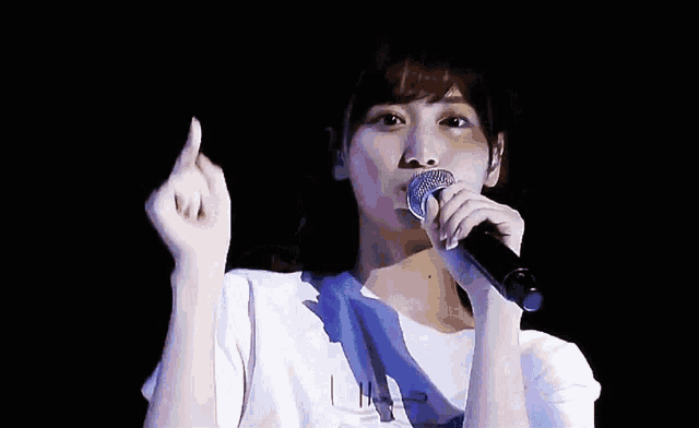 a woman is singing into a microphone and making a heart shape with her hands .