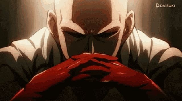 a bald man in a white shirt and red gloves is sitting with his hands folded in front of his face .