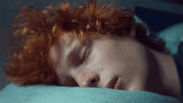 a person with red hair is sleeping on a bed