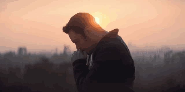 a man praying with his hands folded at sunset
