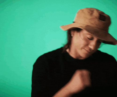 a woman wearing a hat and a black shirt is dancing in front of a green background