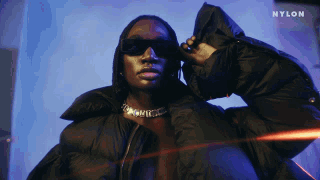 a woman wearing sunglasses and a black jacket with the word nylon on the bottom right