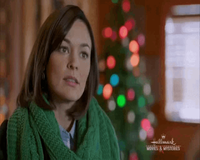 a woman is sitting in front of a christmas tree wearing a green scarf .