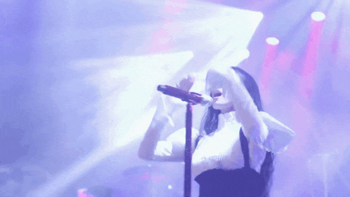 a woman singing into a microphone on a stage with purple lights behind her