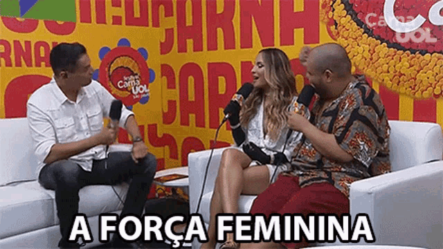 a woman is sitting on a couch talking into a microphone while two men are sitting behind her .