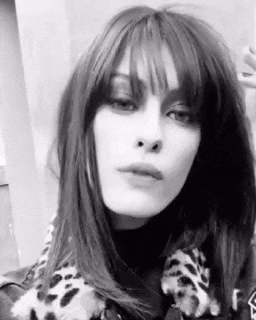 a woman with long hair and bangs is wearing a leopard print jacket and scarf .