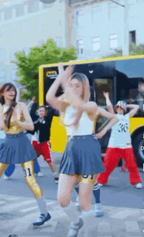 a group of girls are dancing in front of a yellow bus with the number 36 on the side