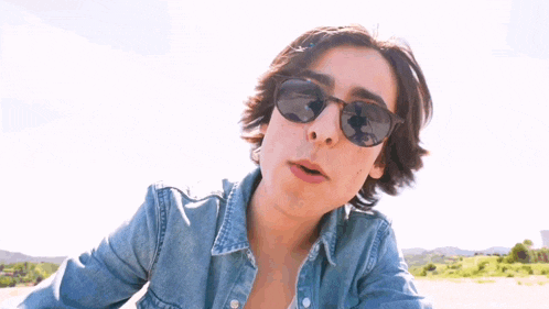 a young man wearing sunglasses and a denim shirt says " happy wednesday "