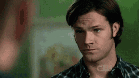 a man in a plaid shirt is looking at another man in front of a green wall .
