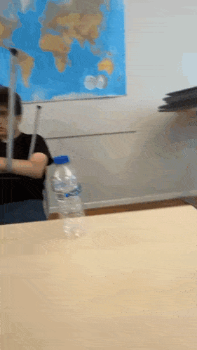 a bottle of aquafina water sits on a table in front of a map of the world