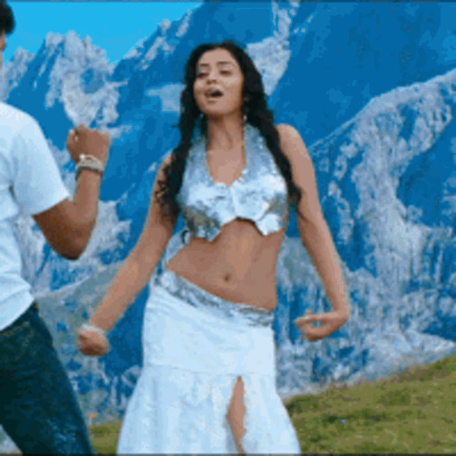 a woman in a crop top and skirt is dancing with a man in a white shirt