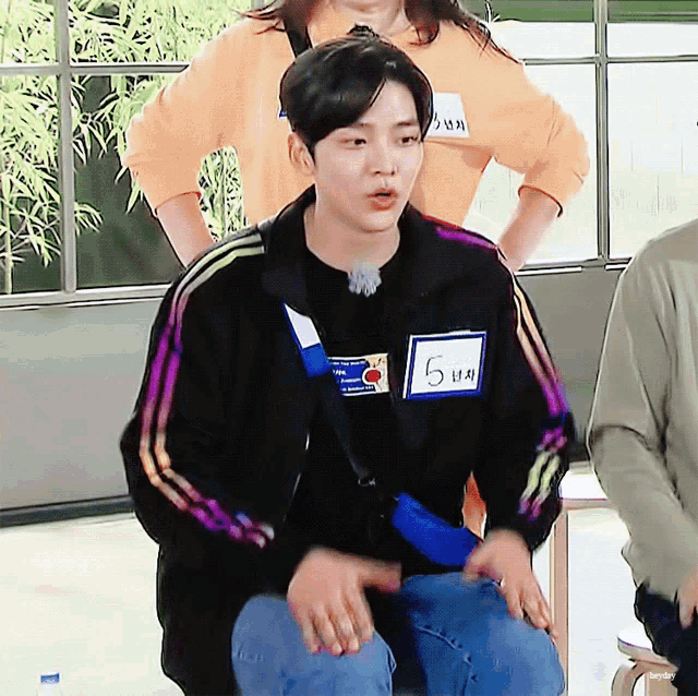 a young man wearing a black jacket has a name tag that says 5 on it