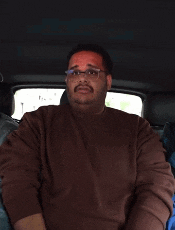 a man wearing glasses and a brown sweater is sitting in a car