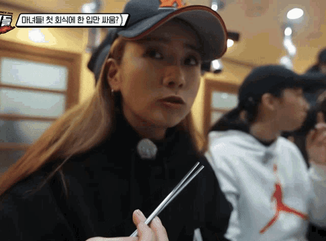 a woman wearing a hat with the letter a on it is holding a pair of chopsticks